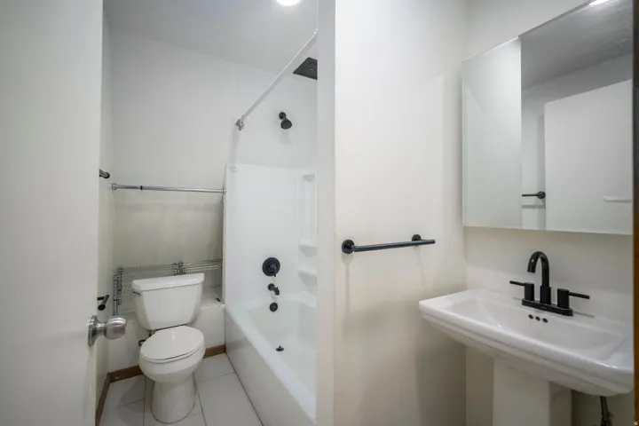 White ceramic pedestal sink with matte black faucet, wall-mounted mirror, and white tiled floor