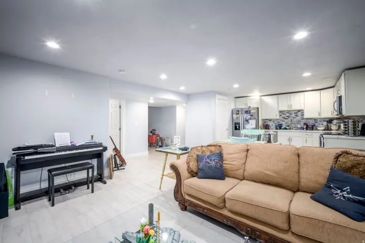 Recessed lighting throughout, wood-finish flooring, white kitchen cabinetry, stainless steel appliances, and a tiled backsplash