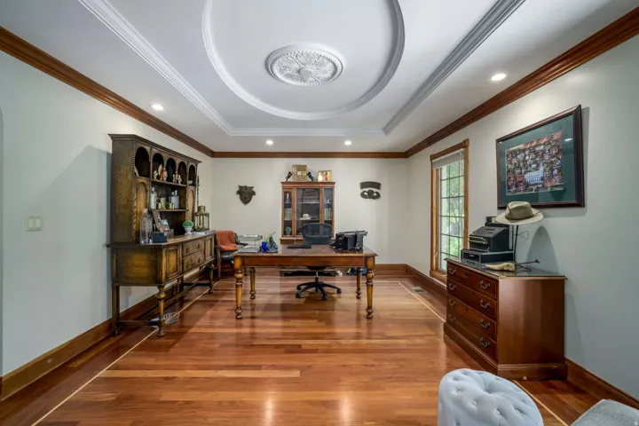 Recessed lighting illuminates the tray ceiling with a decorative medallion, complemented by extensive wood-finish crown molding, wood-finish flooring, and a large window