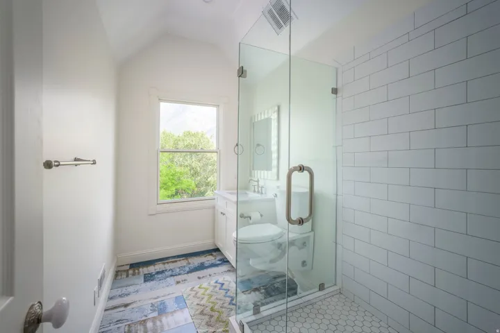 Glass-enclosed shower with subway tile surround, white hex tile flooring, and custom vanity with a vessel sink