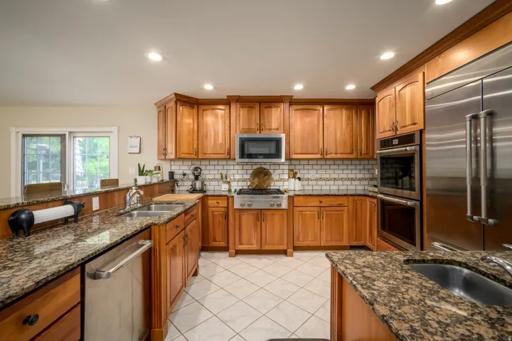 Kitchen featuring wood cabinetry, stainless steel appliances, granite countertops, tile flooring, and a subway tile backsplash