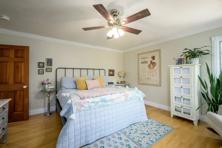 Warm wood-finish flooring, crown molding, and a ceiling fan with integrated lighting