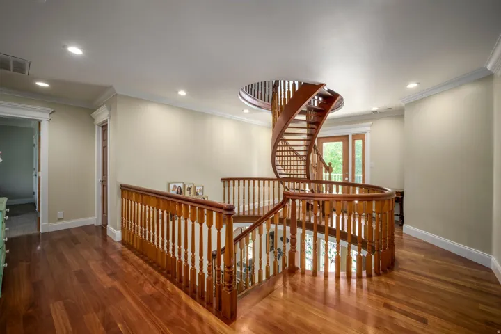 Curved wooden staircase with matching railings, recessed ceiling lighting, wood-finish flooring, and crown molding