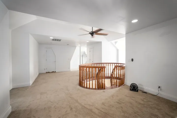 Expansive carpeted loft with an ornate wood staircase railing, recessed lighting, and an overhead ceiling fan