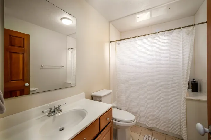 Bathroom featuring a vanity with an integrated sink, wood-finish cabinetry, a wall-mounted mirror, ceramic tile flooring, and a shower with a privacy curtain