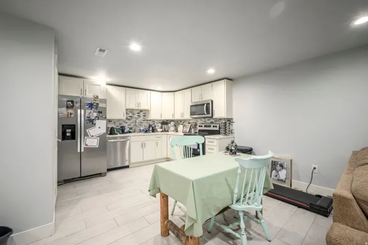 Kitchen featuring white cabinetry, stainless steel appliances, mosaic tile backsplash, and light-toned flooring