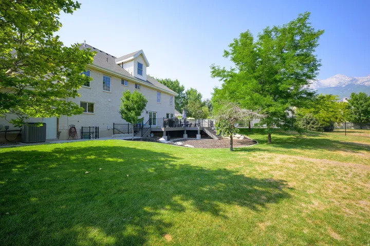 Expansive backyard featuring a manicured lawn, mature trees, a multi-level deck, and a mountain backdrop