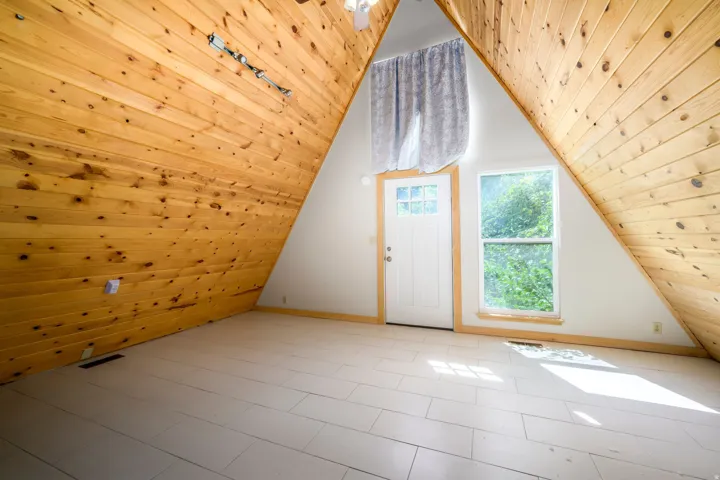 Vaulted wood-paneled ceilings, white painted wood-finish flooring, white entry door with glass panes, single window with wood trim