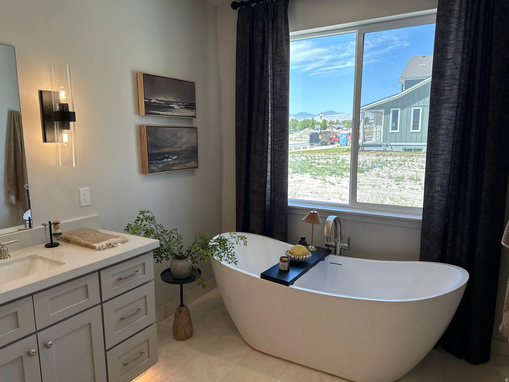 Freestanding soaking tub with chrome fixtures, set against a large window with dark curtains