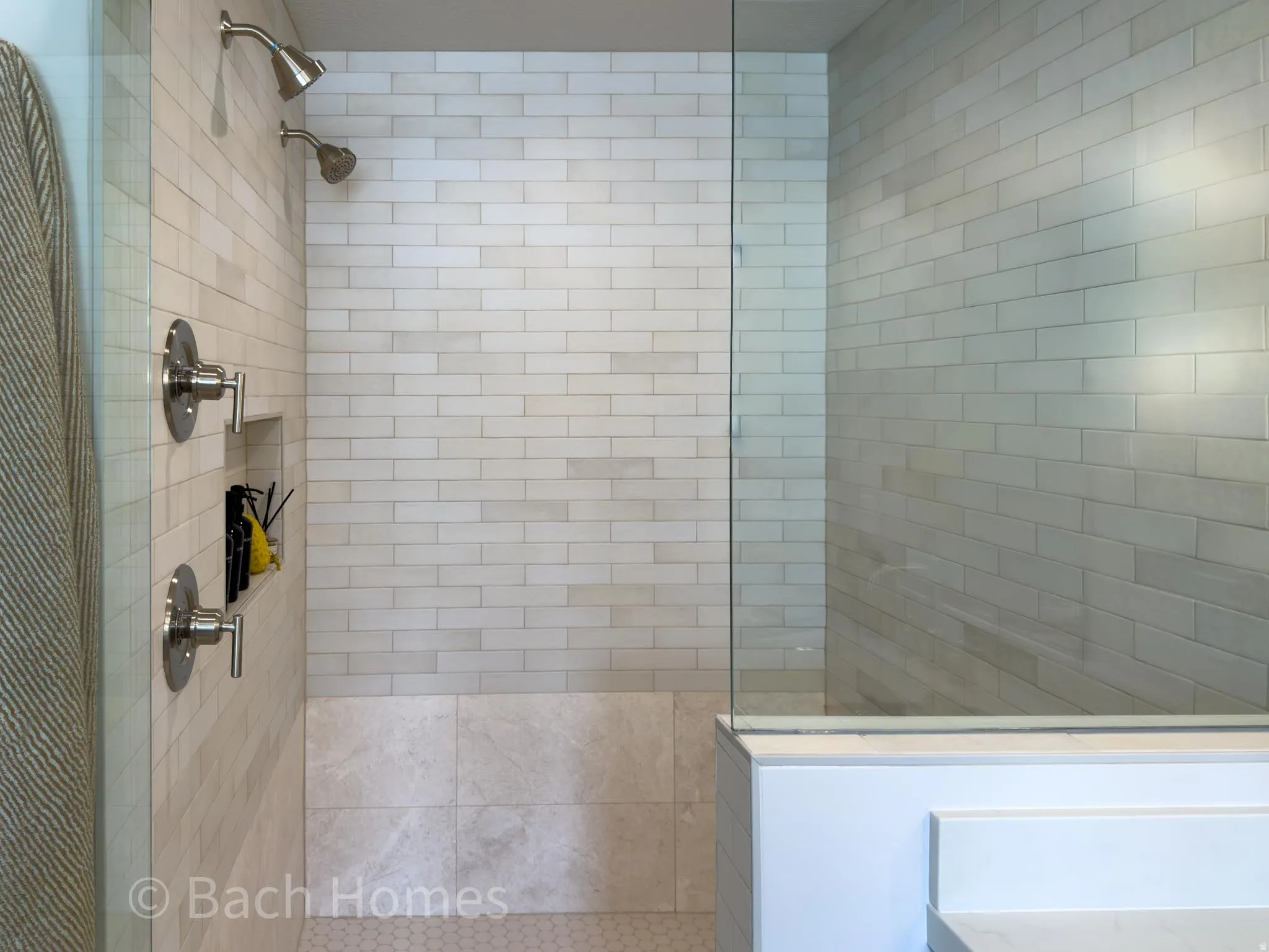 Glass-enclosed shower with subway tile surround, dual shower heads, and an integrated tile niche