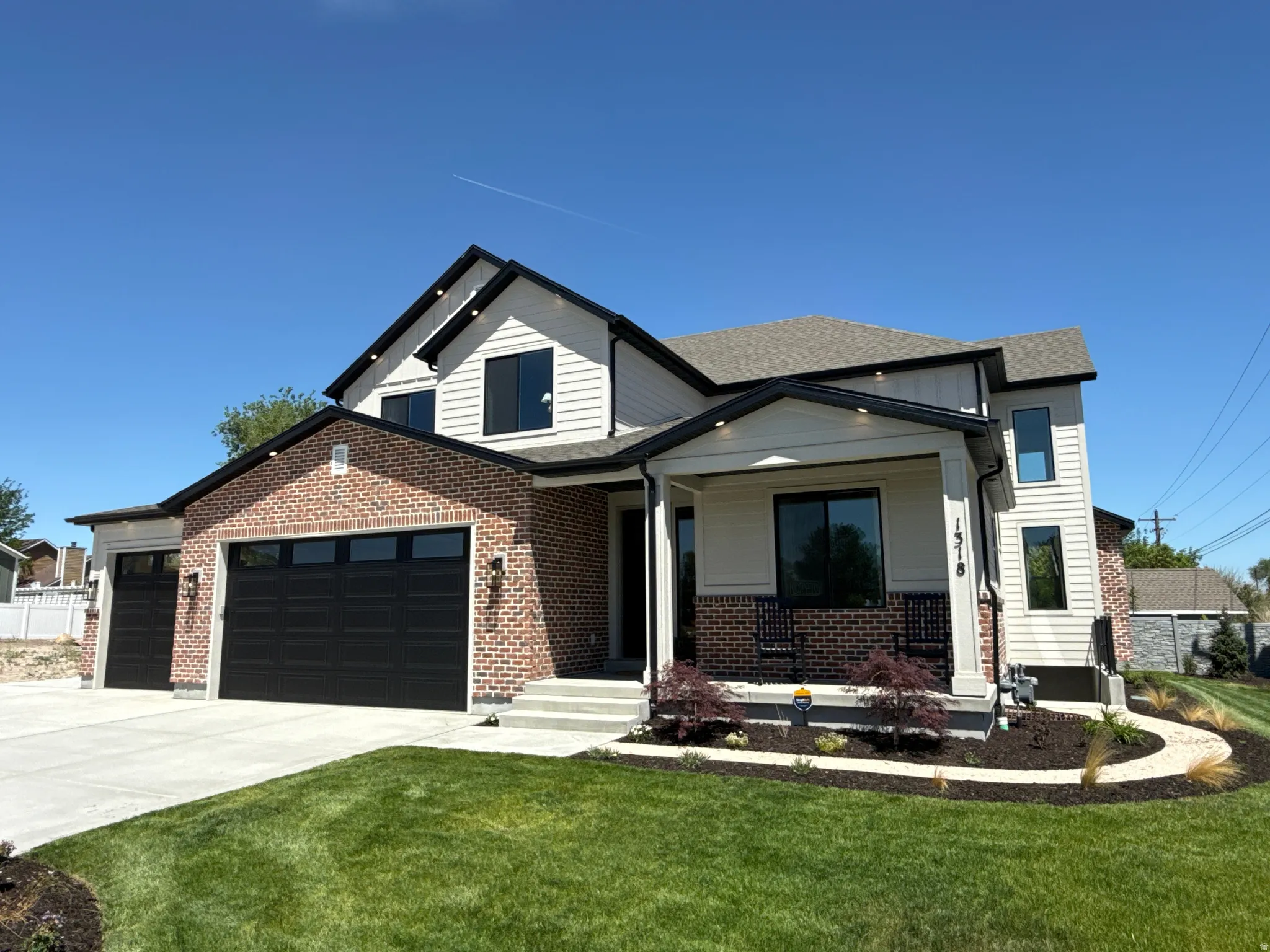 Contemporary exterior featuring brick and siding, a covered front porch, and a two-car garage with black doors
