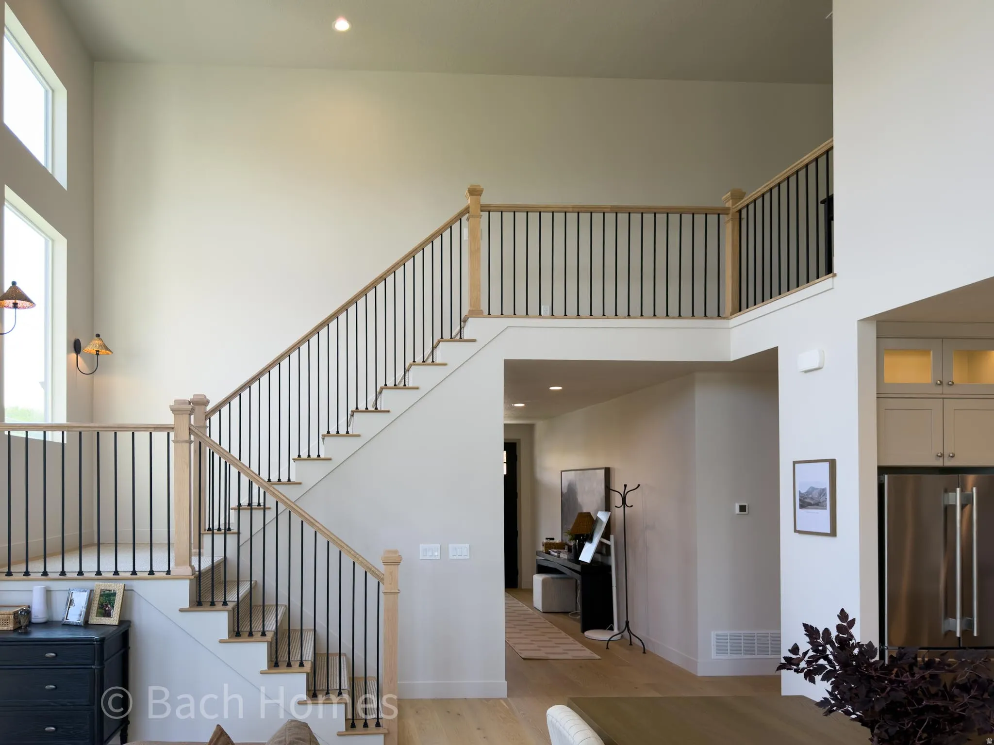 Soaring ceilings with upper-level windows, a two-story staircase featuring wood-finish handrails and black iron balusters, recessed lighting, and wood-finish flooring