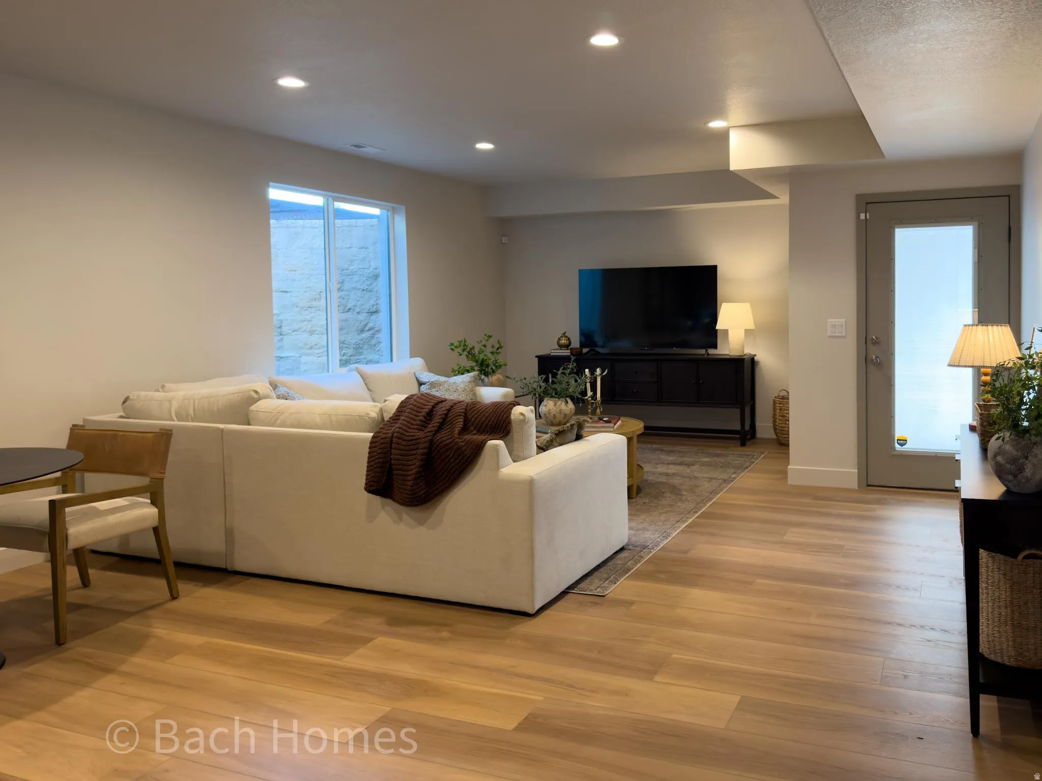 Recessed ceiling lighting, wood-finish flooring, a window well, a ceiling bulkhead, and a frosted glass-paneled door