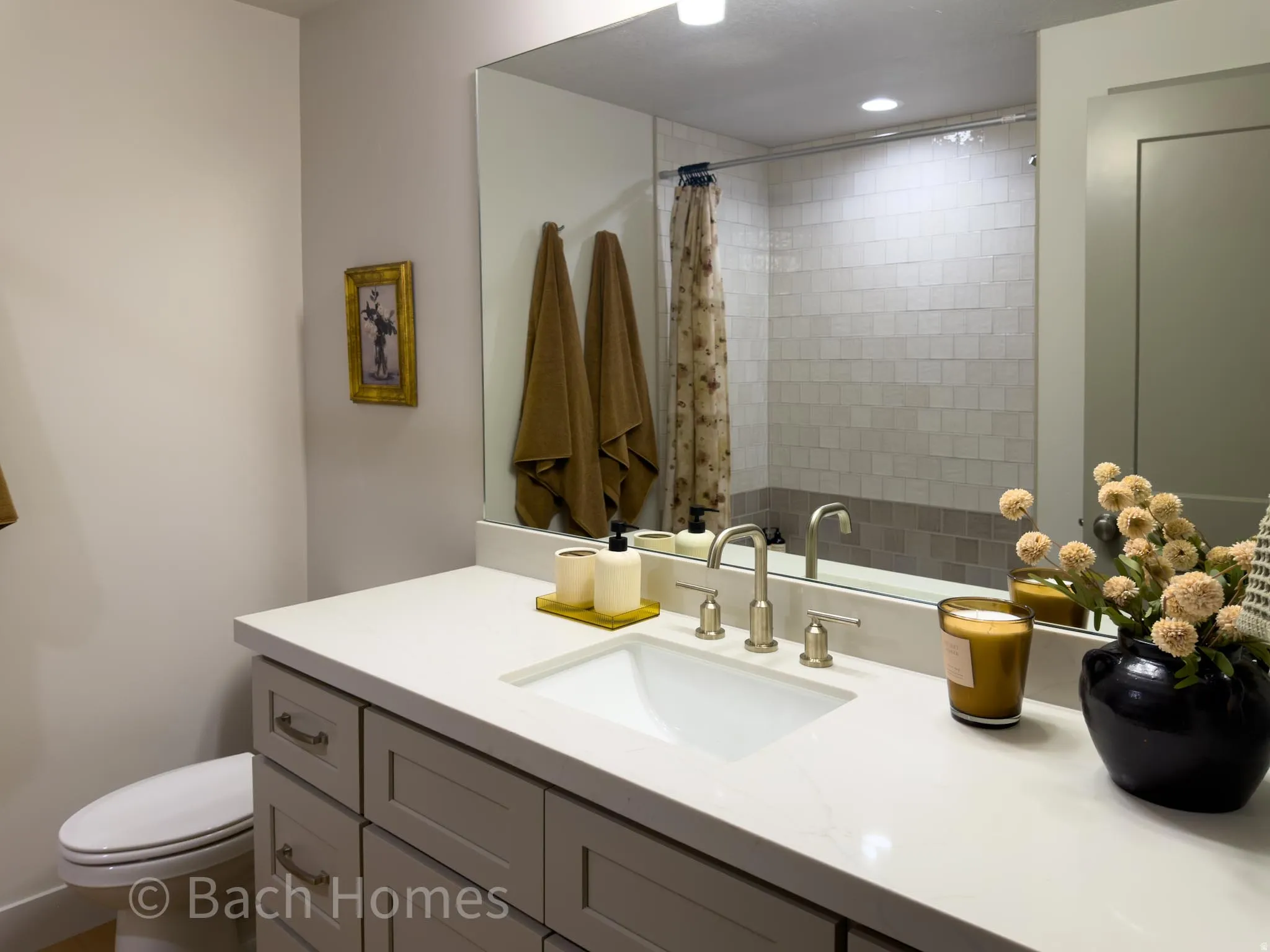 Vanity with a white countertop and integrated sink, brushed nickel faucet, large wall mirror, and a tiled shower-tub combination