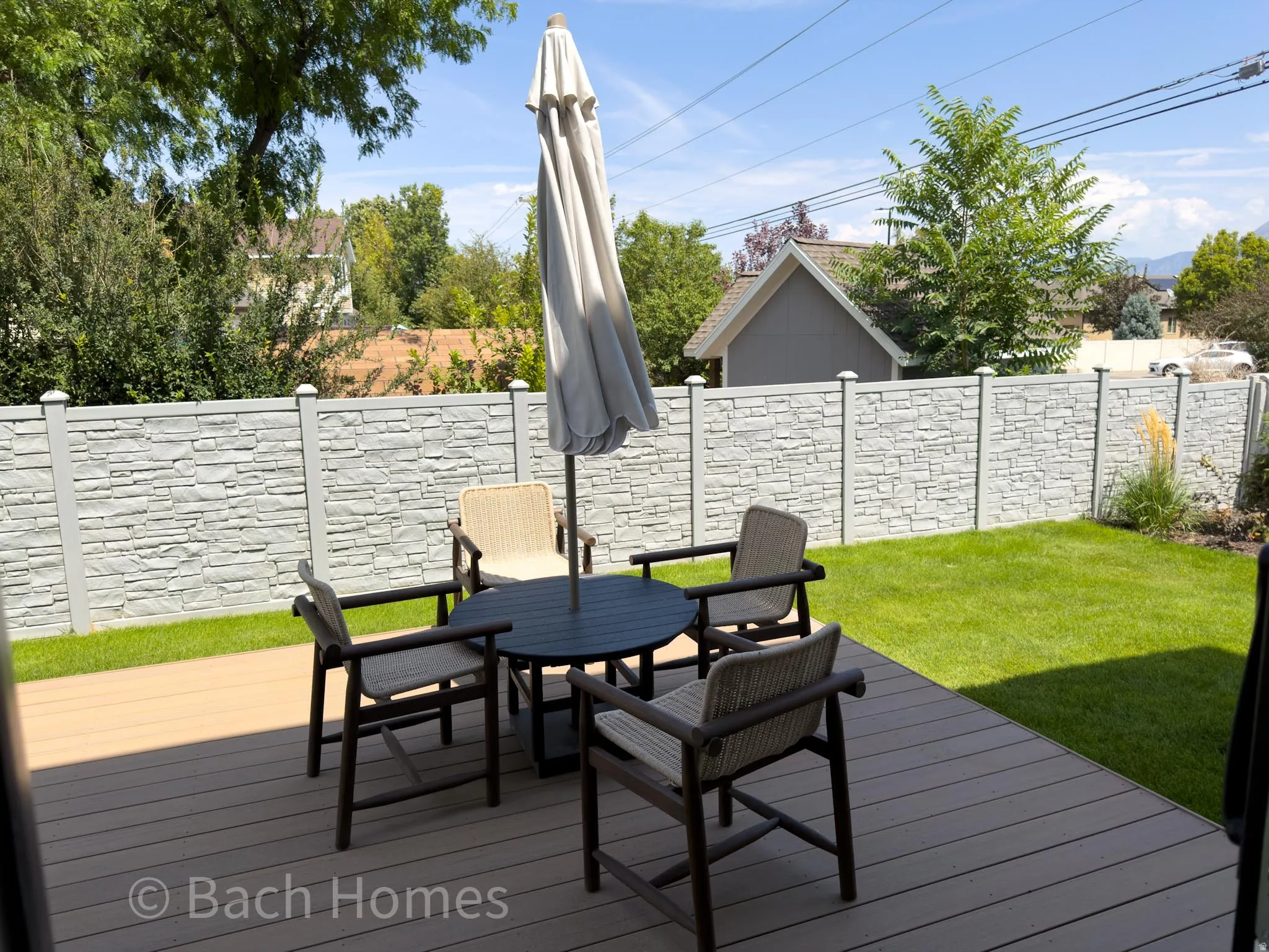 Expansive backyard featuring a composite deck, stone-look privacy fence, and a manicured lawn