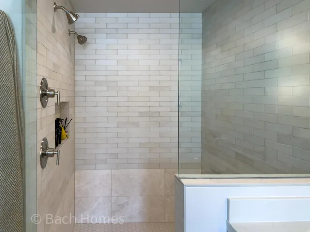 Glass-enclosed shower with subway tile surround, dual shower heads, and an integrated tile niche