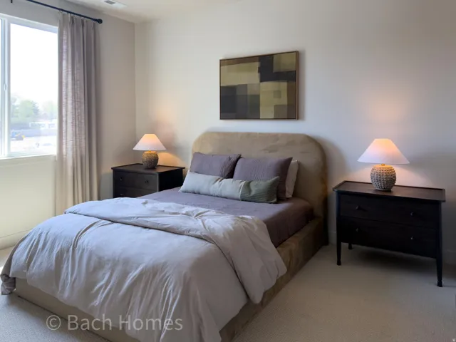 Master bedroom featuring an upholstered headboard bed with coordinating bedding, dual nightstands with table lamps, abstract wall art, and abundant natural light from a large window with thermal-lined curtains