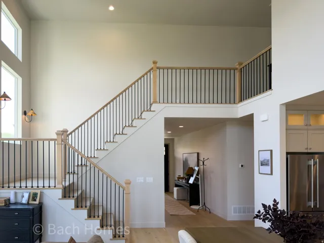 Soaring ceilings with upper-level windows, a two-story staircase featuring wood-finish handrails and black iron balusters, recessed lighting, and wood-finish flooring