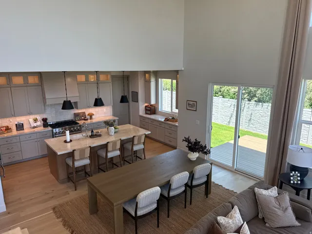 Open-concept living space with wood-finish flooring, a contemporary kitchen featuring light-toned cabinetry, a spacious island with seating, a professional-grade range, and a sliding glass door opening to an outdoor deck and green space