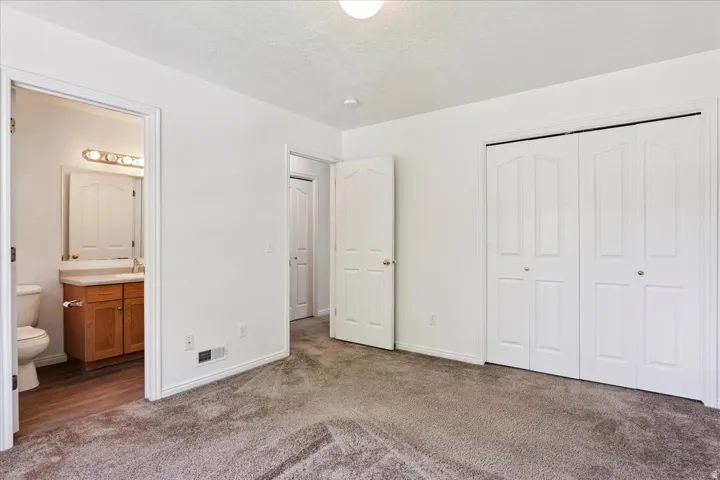 Spacious primary bedroom suite featuring carpet flooring, dual walk-in closets with white six-panel doors, and an ensuite bathroom with wood-finish vanity, ceramic sink, and chrome fixtures