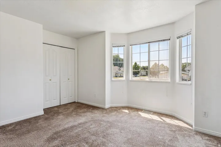 Bright corner bedroom with expansive windows flooding the space with natural light, neutral wall finishes, and soft carpeting throughout