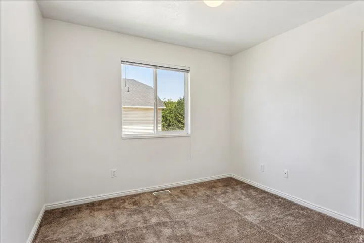 Bright secondary bedroom featuring neutral wall finishes, carpet flooring, and a large double-hung window with natural light and outdoor visibility