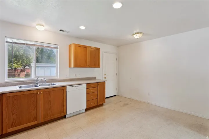 Kitchen area featuring wood-finish cabinetry, a double basin sink, white dishwasher, and recessed ceiling lighting