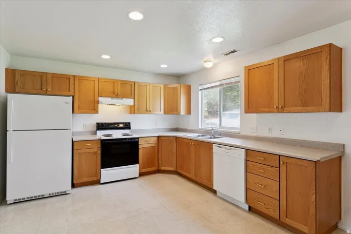 Spacious kitchen featuring warm wood cabinetry, stainless steel appliances, tile countertops, recessed ceiling lighting, and abundant storage throughout the L-shaped layout