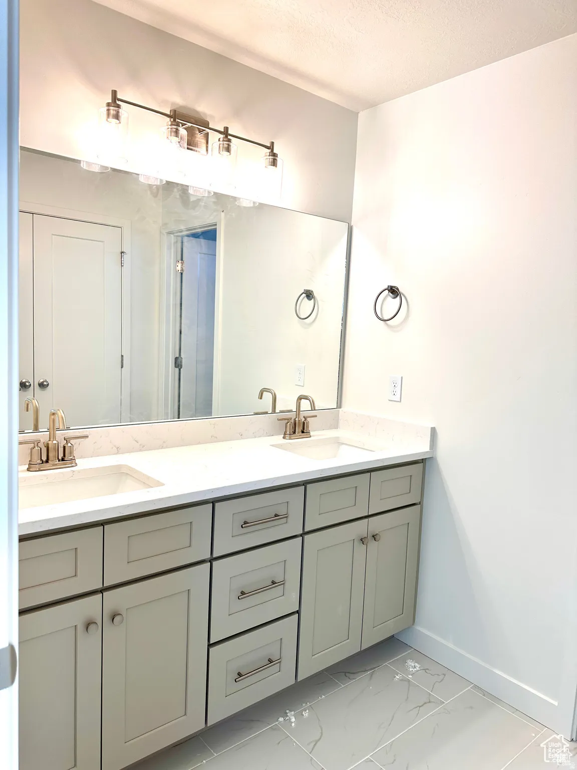 Spa-inspired primary bathroom vanity featuring an expansive double-sink countertop with integrated basin, soft-close cabinetry in sage-finish with brushed nickel hardware, and a large frameless mirror with integrated vanity lighting