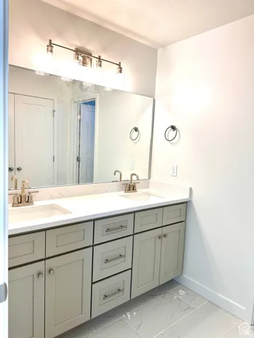 Spa-inspired primary bathroom vanity featuring an expansive double-sink countertop with integrated basin, soft-close cabinetry in sage-finish with brushed nickel hardware, and a large frameless mirror with integrated vanity lighting