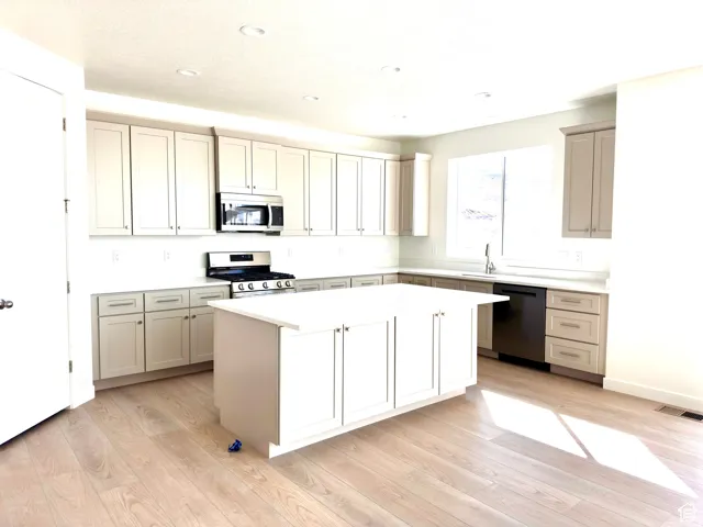 Chef's kitchen featuring white cabinetry with brushed metal hardware, a large center island with additional storage, stainless steel appliances including a gas cooktop and built-in microwave, quartz countertops, a deep undermount sink with chrome faucet,