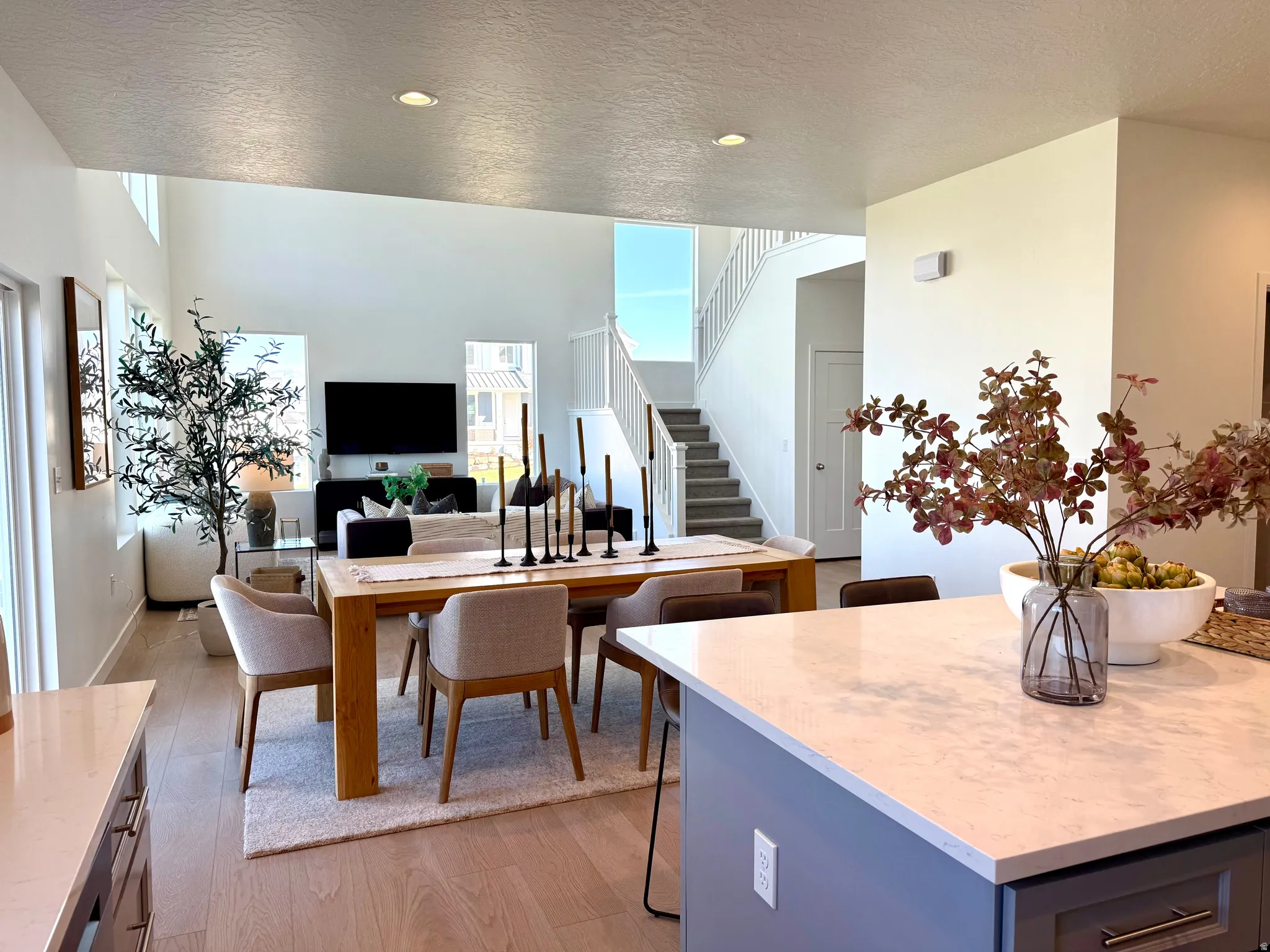 Open-concept living space featuring high ceilings, light wood-finish flooring, and a contemporary staircase with carpeting