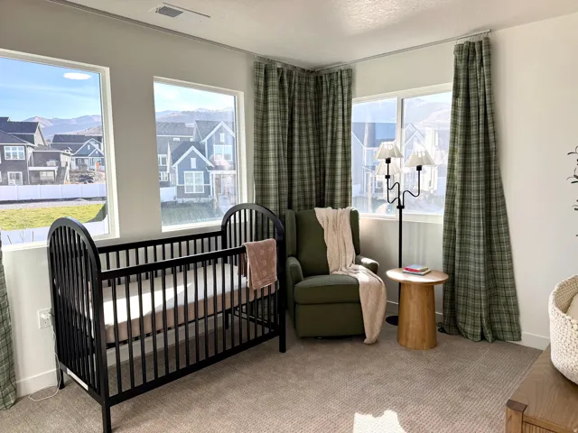 Carpeted room featuring multiple windows with plaid drapes, light-toned walls, and a recessed ceiling vent