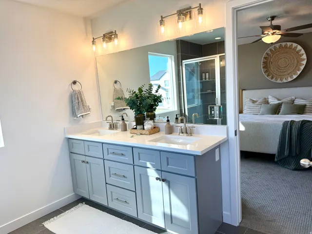 Bathroom featuring a dual vanity with light gray cabinetry and white countertops, brushed nickel fixtures, a spacious mirror, and a glass-enclosed shower with dark gray tile