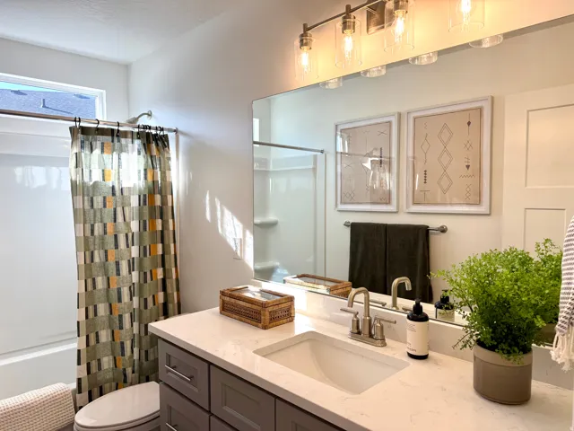 Bathroom featuring a single vanity with a white countertop and undermount sink, a large mirror, and a wall-mounted light fixture with clear glass shades