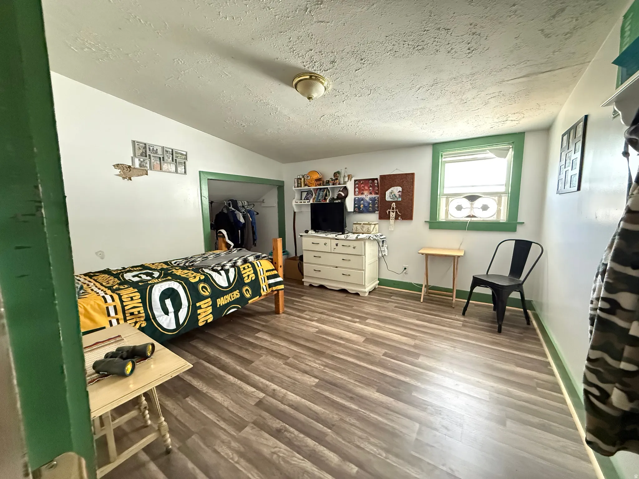 Bright bedroom retreat featuring wood-finish flooring, green-trimmed architectural details, and a green-framed window with natural light