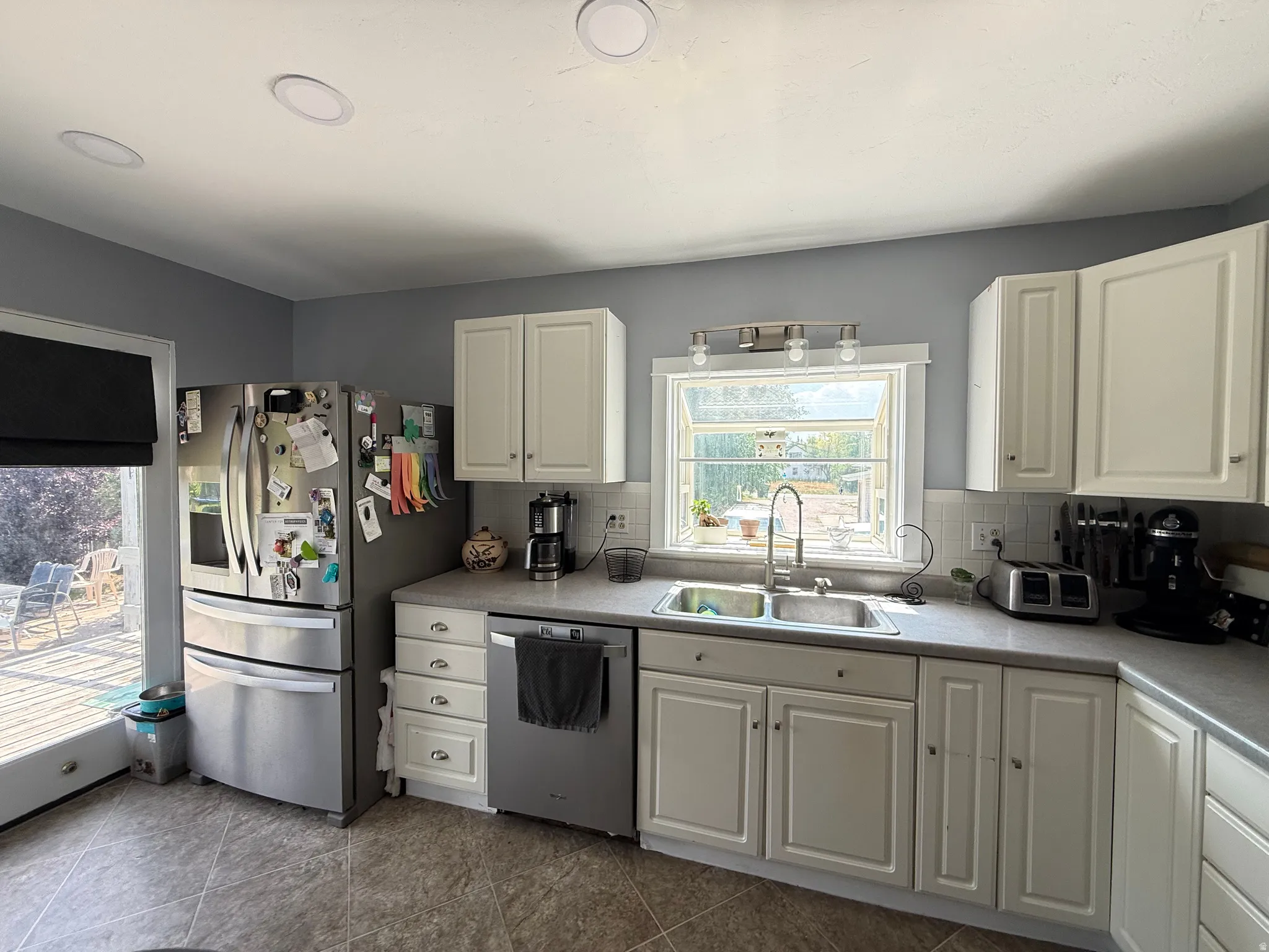 White cabinetry, a stainless steel refrigerator, and a stainless steel dishwasher complement the tiled flooring and recessed ceiling lighting
