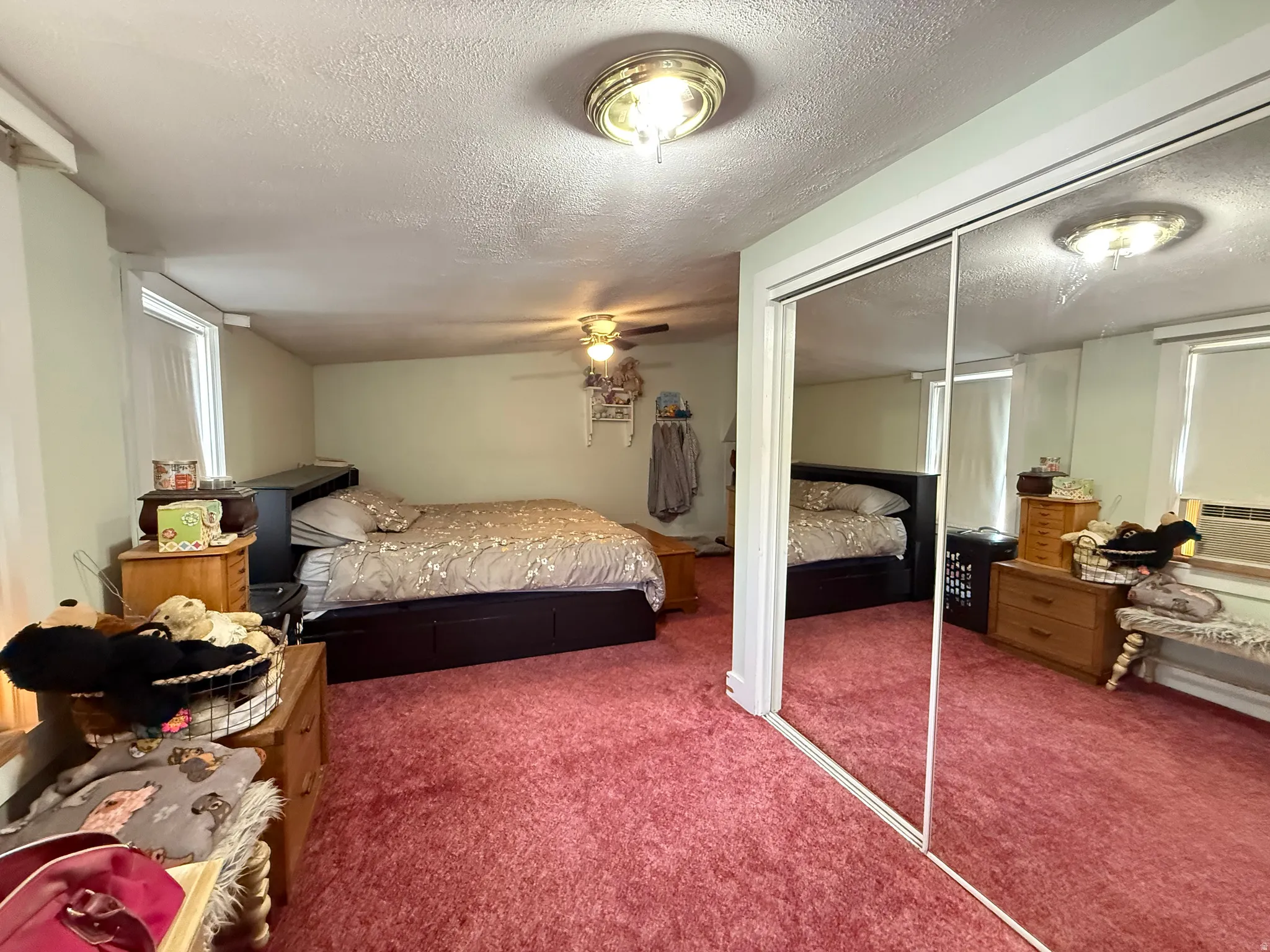 Spacious primary bedroom suite featuring mirrored sliding closet doors, recessed ceiling lighting, warm carpeting throughout, and an attached dressing area with ample storage and natural light from street-facing windows