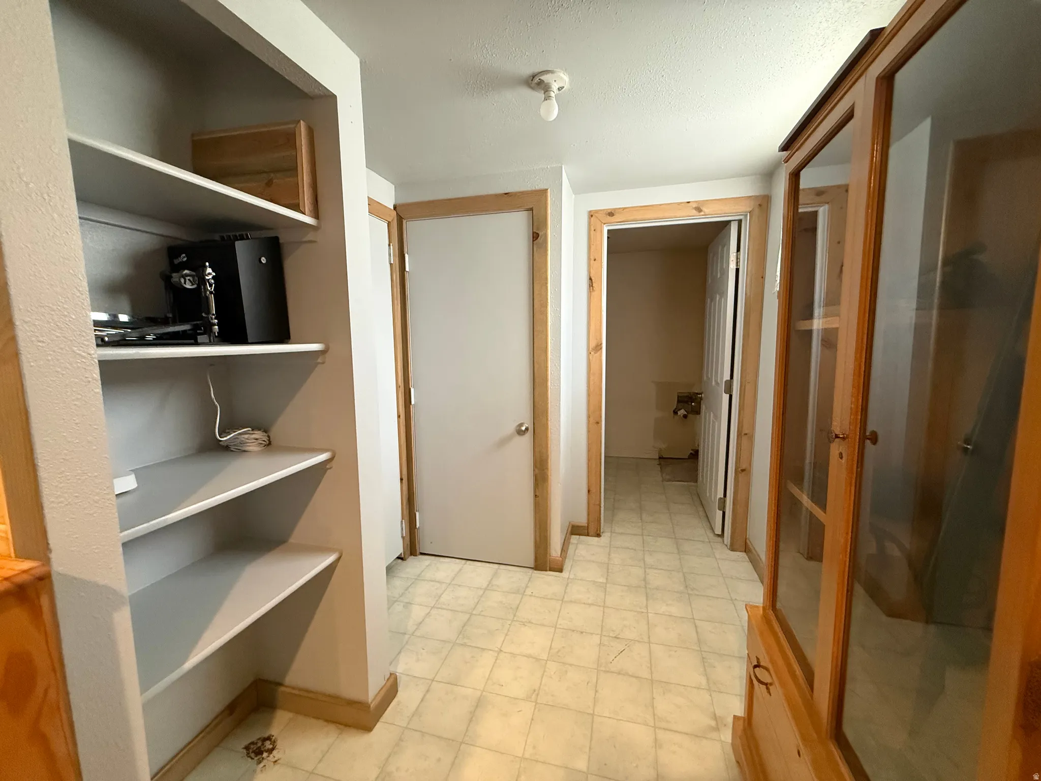 Hallway featuring built-in shelving with adjustable shelves, wood-finish framing throughout, ceramic tile flooring, and multiple wood-finish doors providing access to adjacent spaces
