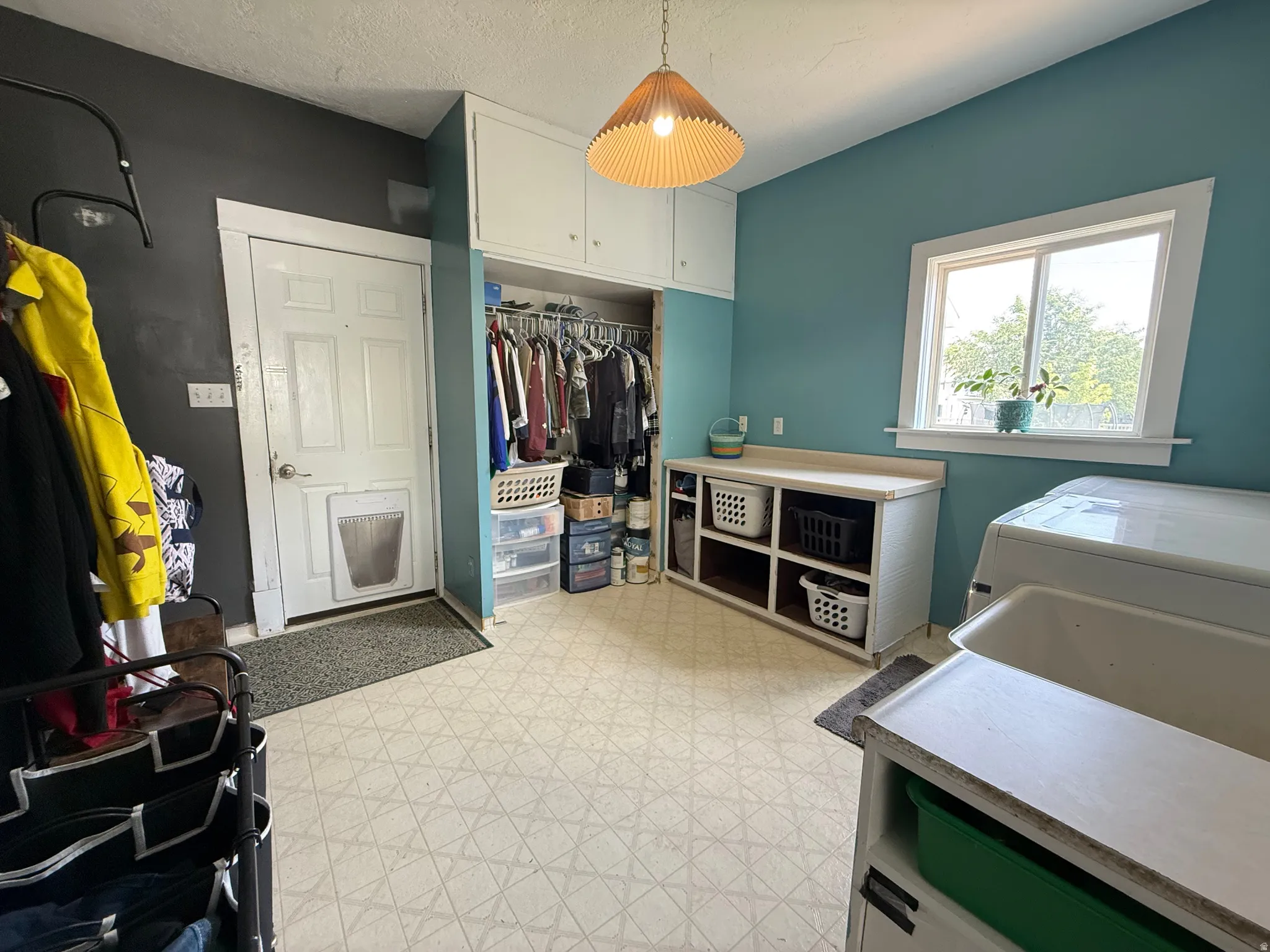 Spacious laundry room featuring ceramic tile flooring, built-in cabinetry with open shelving, a pendant light fixture, and large front-loading appliances