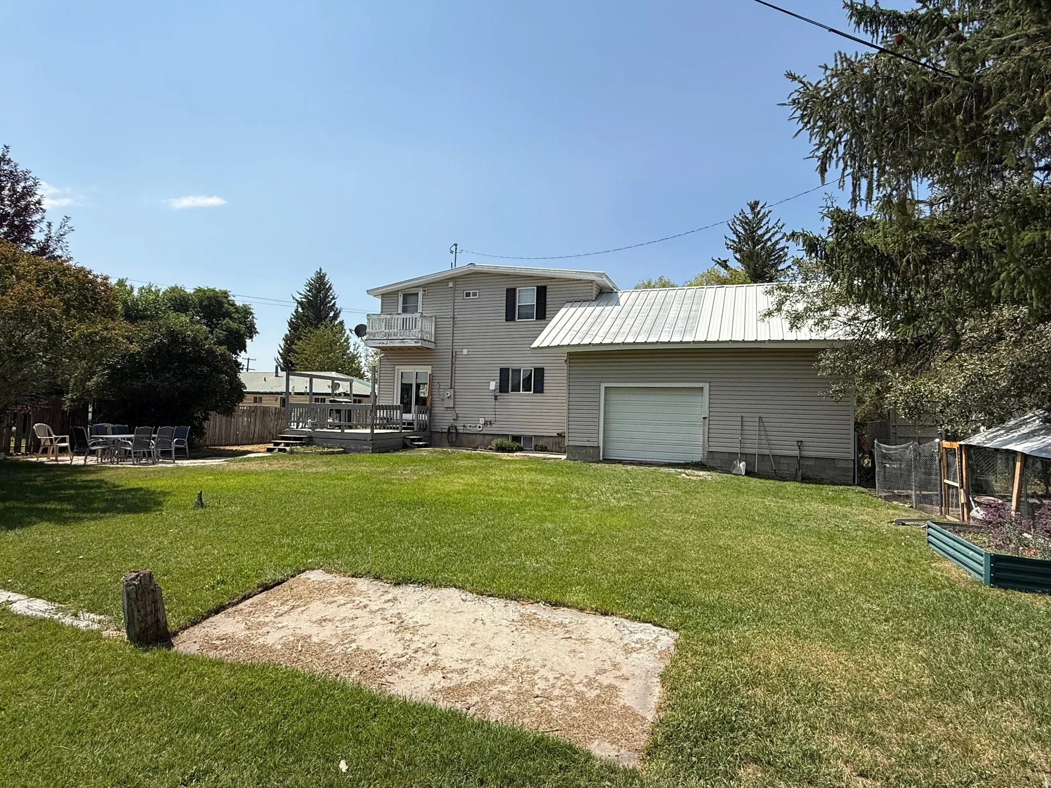 Expansive green lawn with a wood deck, balcony, detached garage with metal roof, and raised garden beds
