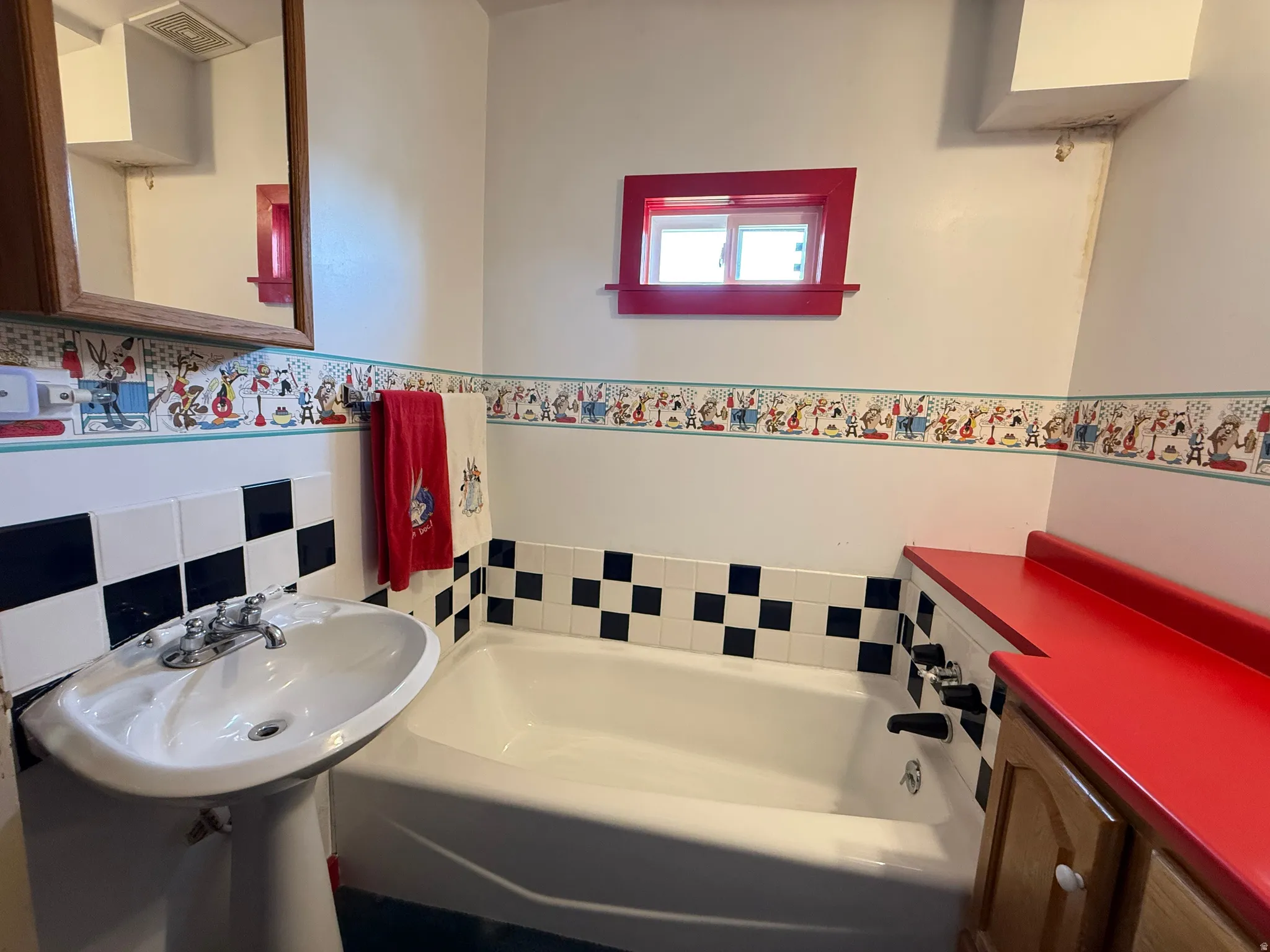 Charming bathroom featuring a classic black and white tile design with coordinating diamond pattern accent, pedestal sink, and built-in soaking tub with tile surround