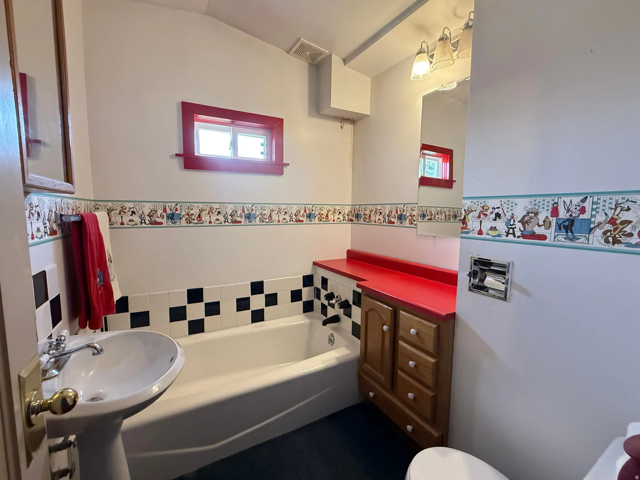 Pedestal sink, built-in bathtub, checkerboard tile surround, wood-finish vanity with red countertop, and a window with red trim