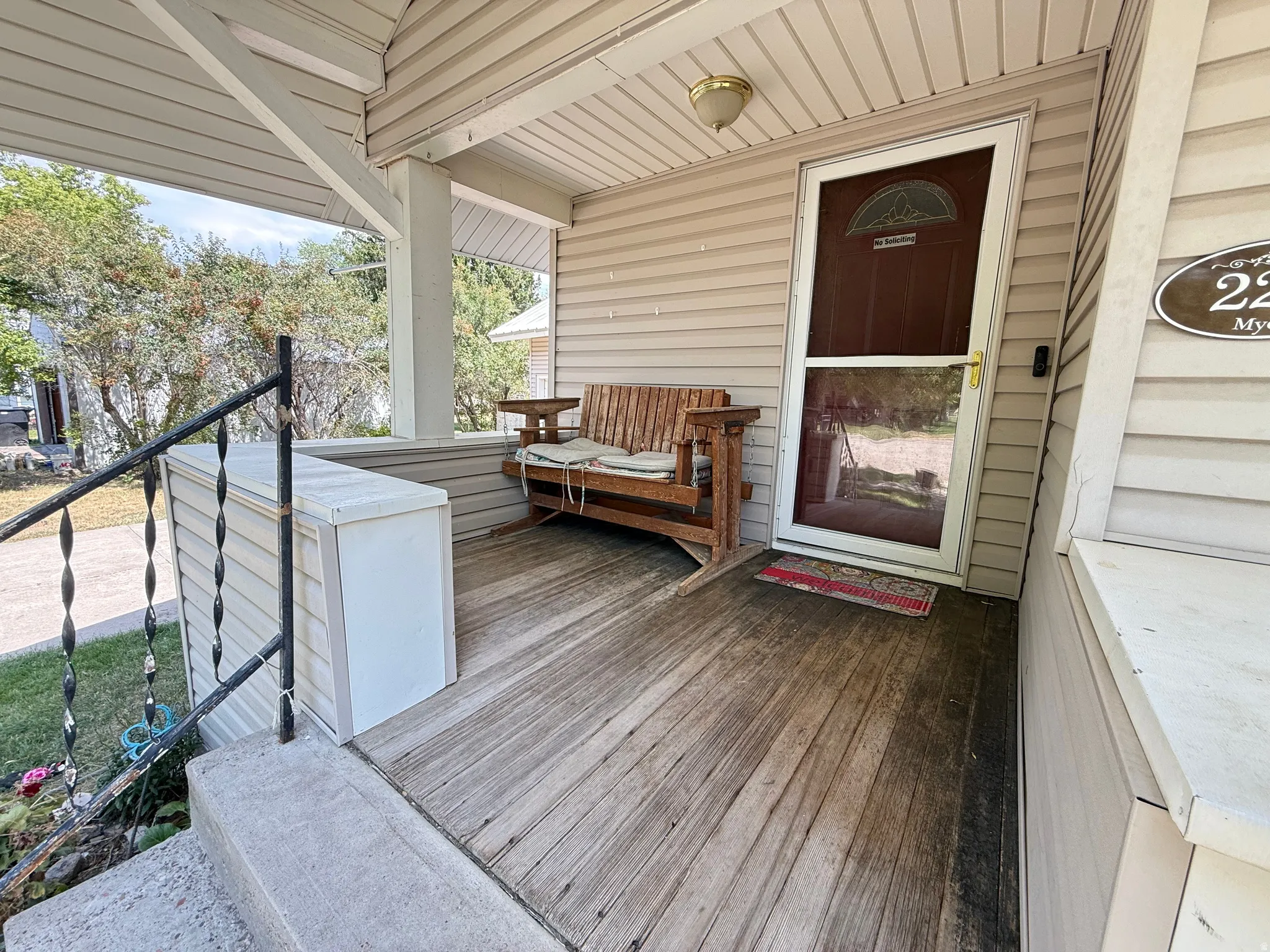 Welcoming front porch featuring a wood-finish deck, metal railing with cable detailing, covered ceiling with recessed lighting, wooden bench seating, and direct entry through a dark-stained entry door