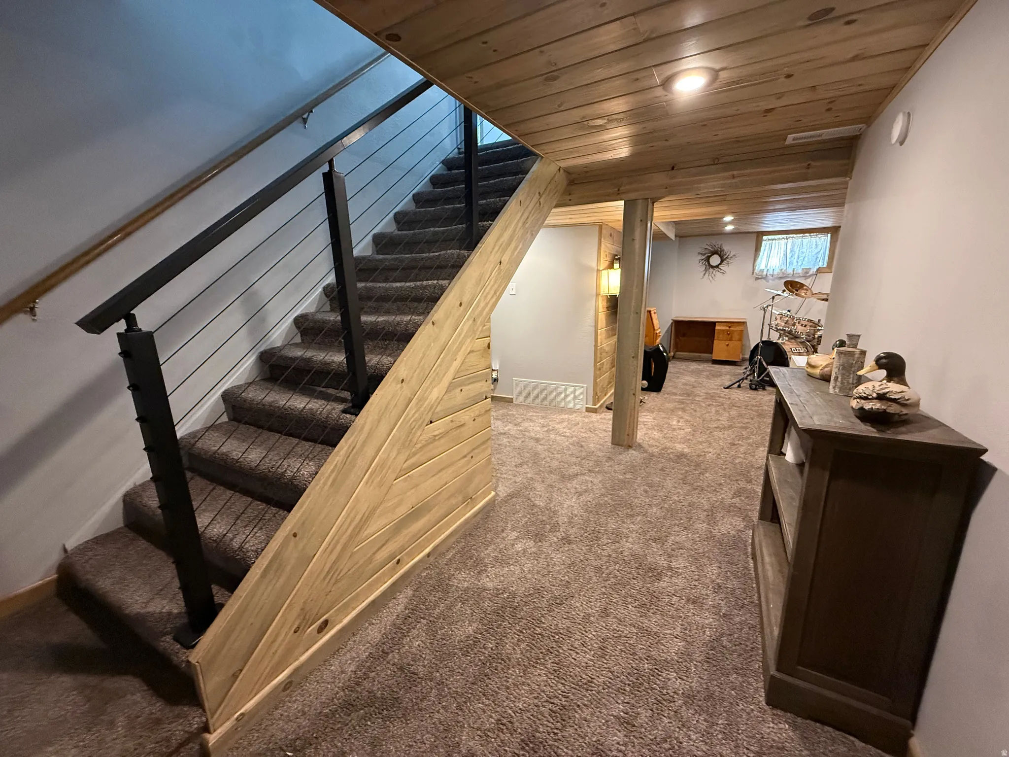 Carpeted stairway with modern cable railing, wood-finish ceiling, and shiplap-style wall accents