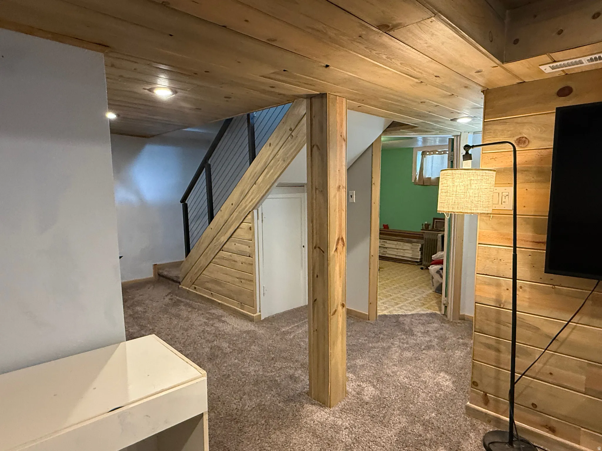Wood-paneled ceiling, wood-paneled accent wall, wood-finish support beam, carpet flooring, cable railing