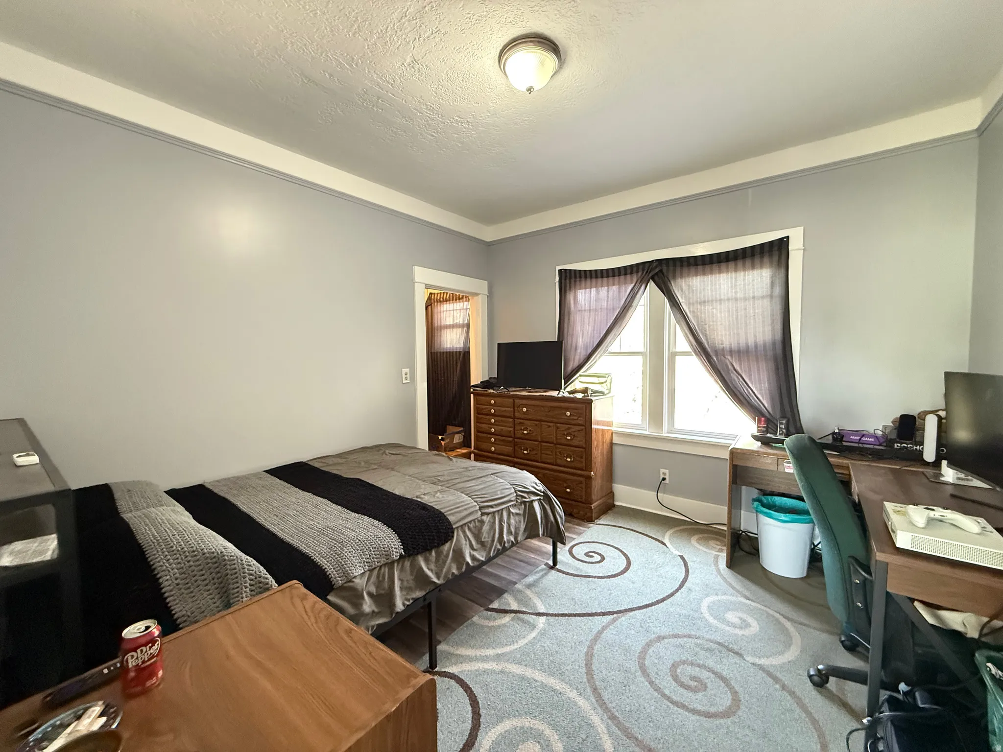 Spacious bedroom featuring neutral wall finishes, carpeted flooring with geometric patterning, recessed ceiling lighting, and ample natural light from a large window with vertical blinds
