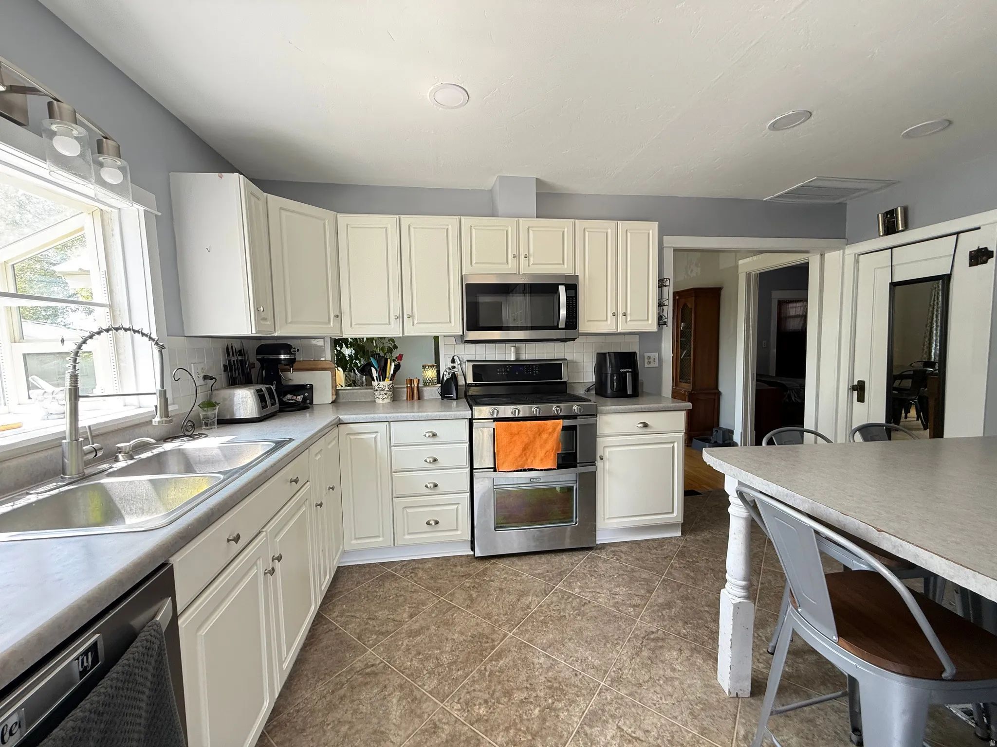 Kitchen featuring white cabinetry, stainless steel appliances, a double basin sink, and tile flooring