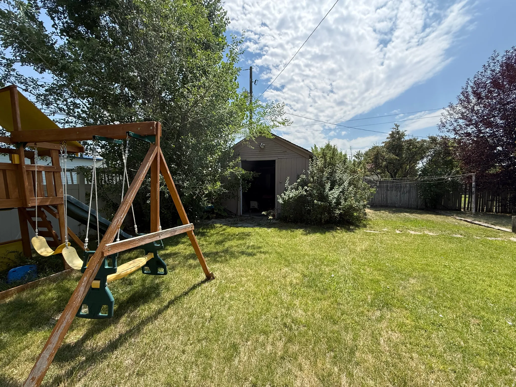 Expansive backyard featuring a lush lawn, mature trees, wood-fenced perimeter, and a detached storage shed