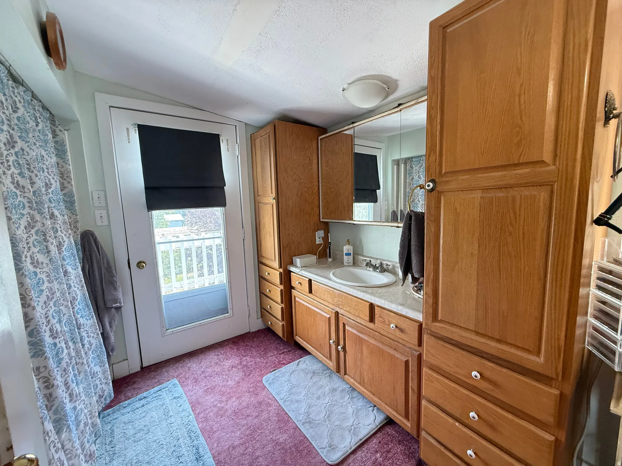 Primary Bathroom featuring wood-finish cabinetry with abundant storage, a ceramic sink with chrome fixtures, and a large mirrored medicine cabinet
